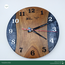 Load image into Gallery viewer, Bring timeless style to your space with &quot;Cael&quot;, a 12-inch round wall clock that blends elegant design with industrial charm. Handcrafted using a unique combination of wood, resin, and acrylic, this statement piece adds depth, character, and modern sophistication to any room.

Perfect for home interiors, office walls, or business spaces, Cael doesn’t just tell time — it tells your story. With options for custom engraving or logo placement, it also makes a standout choice for corporate gifts, housewarming pre
